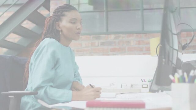 Vertical video: Writing woman in teal top watching monitor displaying, writing in notebook at loft