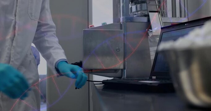 Lab tech placing gloved hands on instrument calibrating device, logging data on laptop for test