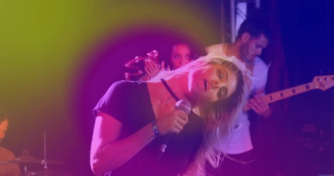 Camera rising revealing lead singer singing music for crowd, neon lights accenting mic guitar drums
