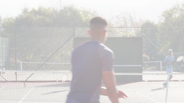 Front man swinging racket, initiating tennis rally in friendly match, ball crossing net amid flare