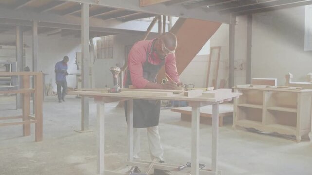 Carpentry worker measuring, planing plank at bench with helpers arriving holding frame to fit joint