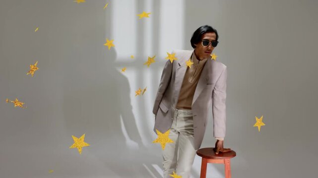 Vertical video: Stepping man posing as stars appearing, touching stool, adjusting blazer in studio