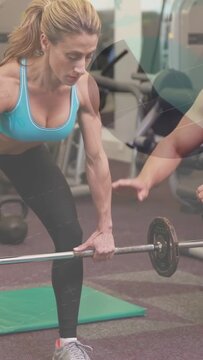 Vertical video: Trainee approaching barbell on gym mat trainer stepping and guiding pull for safety