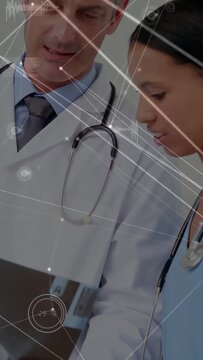 Vertical video: Doctor tapping tablet, nurse leaning, reviewing medical data with HUD overlays