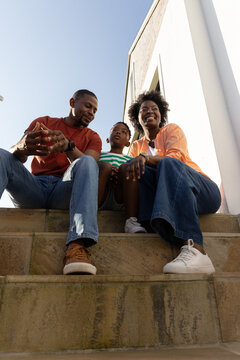 African American family with child sitting on stone steps beside white building, wearing sneakers