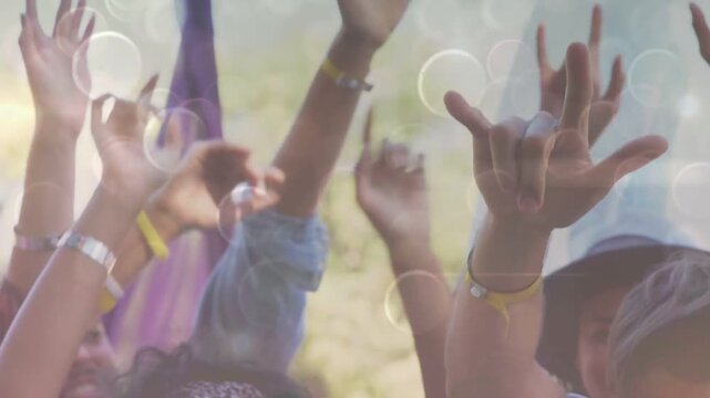 Event crowd reacting to music beat, raising hands and forming signs with bokeh overlay over hands