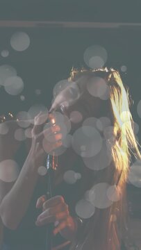 Vertical video: Singer holding mic, singing, tossing hair by drum beat driving music, bokeh overlay