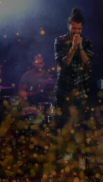 Vertical video: Singer gripping mic singing music to move crowd, drummer keeping beat, bokeh rising