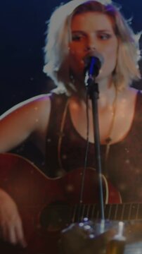 Vertical video: Spotlight cueing singer playing guitar, light flecks lit face, engaging music fans