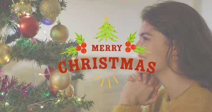 Animation of merry christmas text banner over caucasian woman looking at a decorated christmas tree