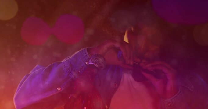 Musician forming heart shape then aligning harp to mic, playing music riff under red violet haze