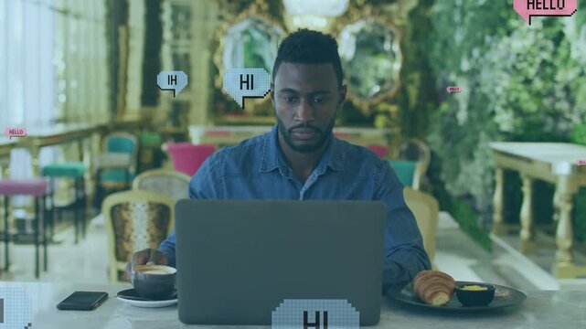 Animation of hi and hello speech bubbles over african american man using laptop and drinking coffee