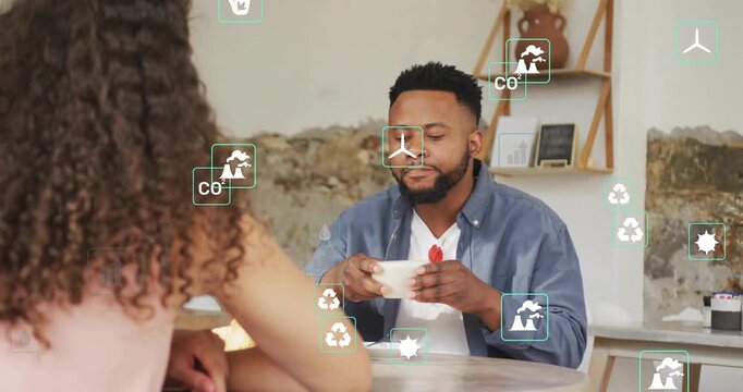 Vertical video: Man sipping cup at cafe, pausing then explaining eco data with icons overlapping