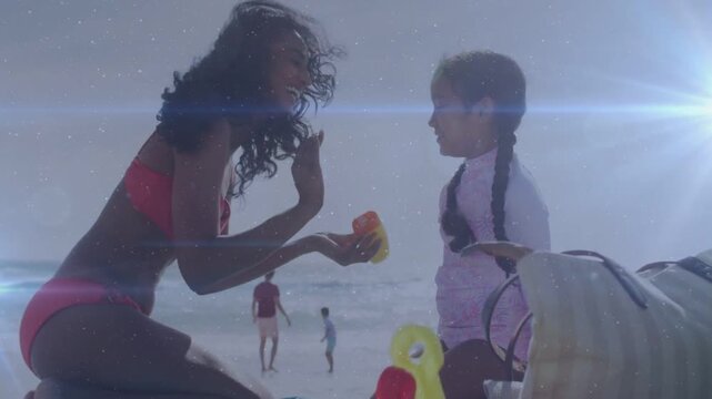 Woman kneeling reaching bottle applying sunscreen for health to girl, protecting from sun on beach