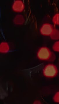 Vertical video: Lead music singer playing guitar moving to mic singing as bokeh refracts over face