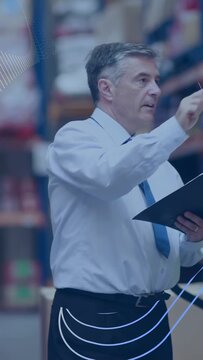 Vertical video: Warehouse mgr pointing, checking clipboard and noting racks while wave overlaying