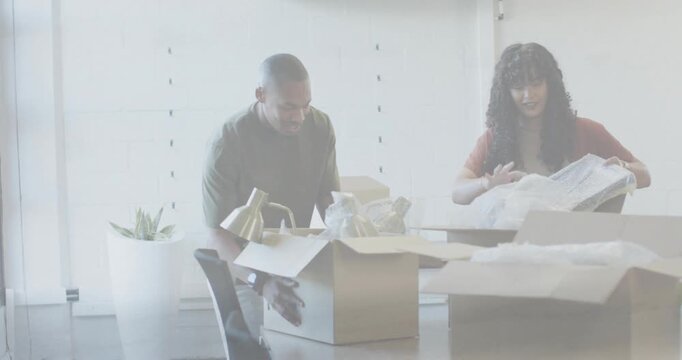 Coworkers opening boxes and unpacking brass lamp and framed piece, arranging workspace for setup
