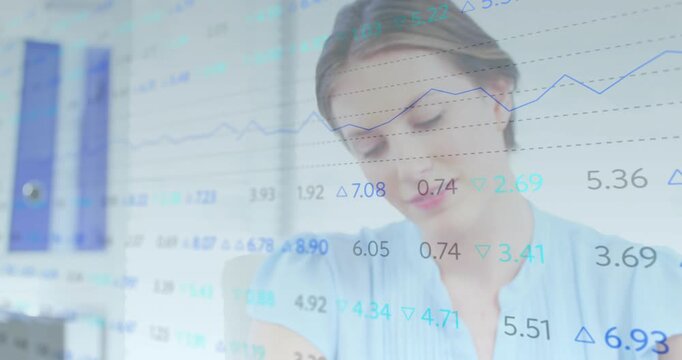 Woman writing notes at desk with translucent finance numbers and charts shifting, spurring analysis