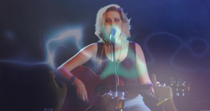 Vertical video: Pulling focus musician strumming guitar and singing to mic on stage for crowd hands