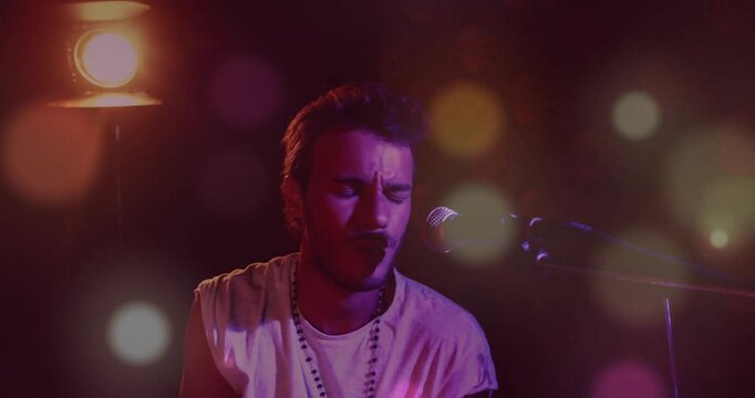 Artist raising stick, hitting beats and singing into mic, emoting while bokeh flares moving onstage