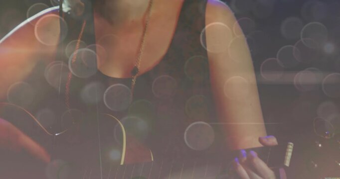 Teen musician playing guitar, singing to mic live, camera pulling back revealing bokeh veiling face