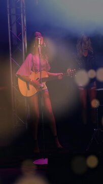 Vertical video: Singer starting strum, performing music at retro mic while lights fog making bokeh