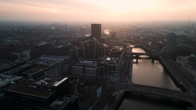 Aerial view dollying in - The modern business centre of Dublin in the shore of Liffey River, bridges all long the way in a foggy sunset evening. - Dublin, Ireland