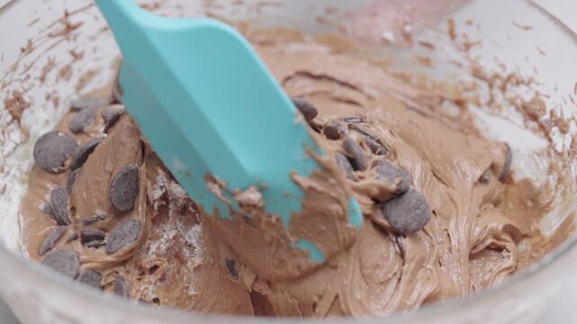 Close up of chocolate chip cookie dough being mixed with spatula showing thick texture and ingredients