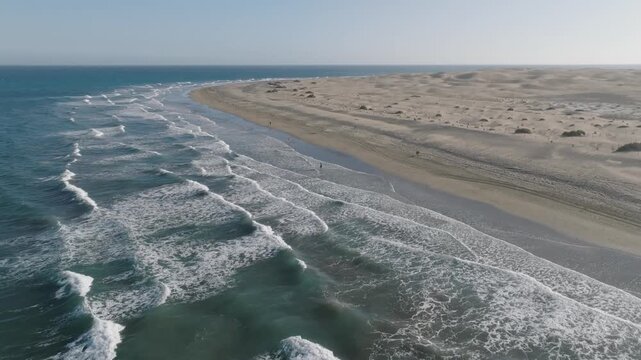 Drone pullback over the untouched tip of Maspalomas beach in Gran Canaria, Spain, revealing waves, shoreline, and vast natural dunes with no buildings.