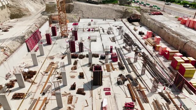 Aerial view of construction site with concrete foundation, columns and building materials. Industrial development process with cranes and structure base in progress, urban infrastructure scene.
