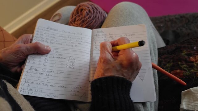 Elderly hands carefully guide a pen across a notebook, meticulously documenting a crochet pattern. The ink flows steadily as she records each stitch and row in her personal, handwritten guide.