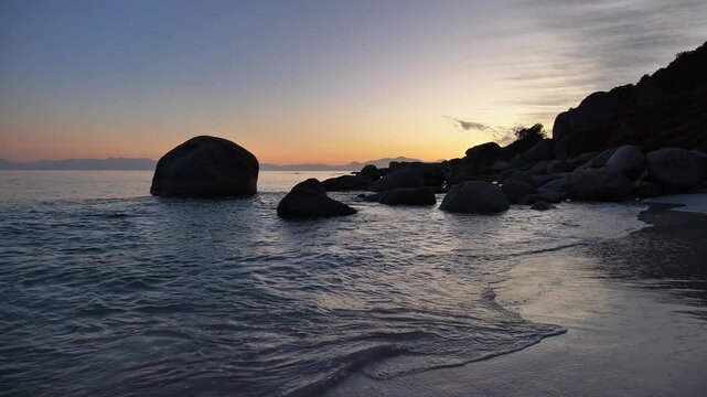 Golden hour sunrise paints the sky with soft colours over a tranquil ocean shoreline dotted with large boulders and gentle waves at Millers Point, Simon's Town.