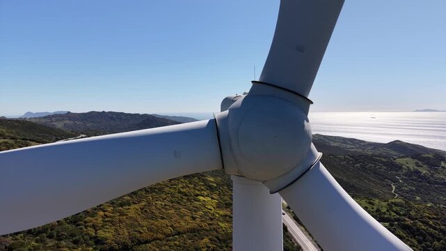 Close-up drone shot rotating around the hub of a wind turbine, with the straits of Gibraltar in the background