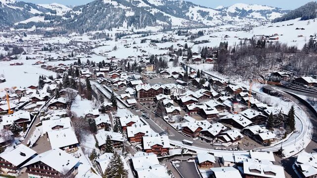 Aerial: downtown Gstaad snowy cityscape during the day in Canton of Bern, Switzerland, orbit drone shot