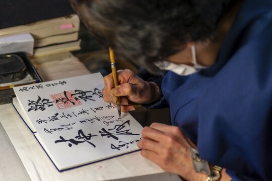 Woman writes Japanese characters, calligraphy, lucky charms to buy in Todaiji Temple, Japan, Nara, Japan