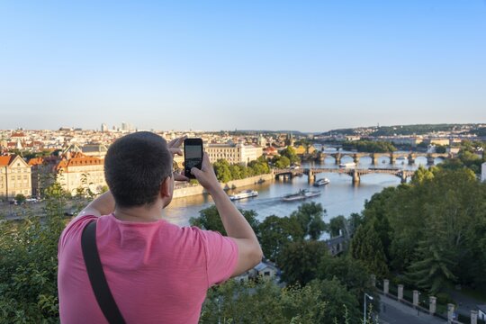 Tourist photographing with smartphone, city view with view to bridges over river Vltava, Prague, Bohemia, Czech Republic