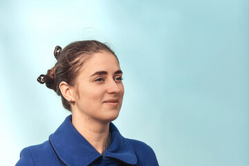 Young woman in blue coat looking thoughtful in a clean pastel portrait with a hair bun © Nataliia