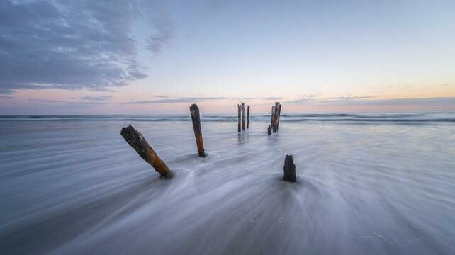 Old broken bridge, posts in the water on the beach at dusk, St. Clair, Dunedin, Southland, New Zealand