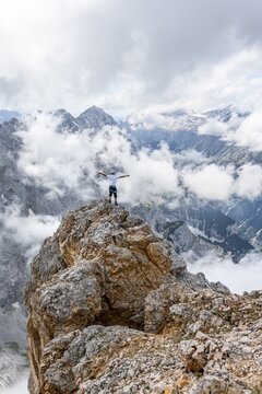 Hiker standing on a rock, at the summit of the Partenkirchner Dreitorspitze, view into the Reintal valley to cloudy peaks, in the background Zugspitzplatt and Zugspitze, Wetterstein Mountains, Garmisch Partenkirchen, Bavaria, Germany