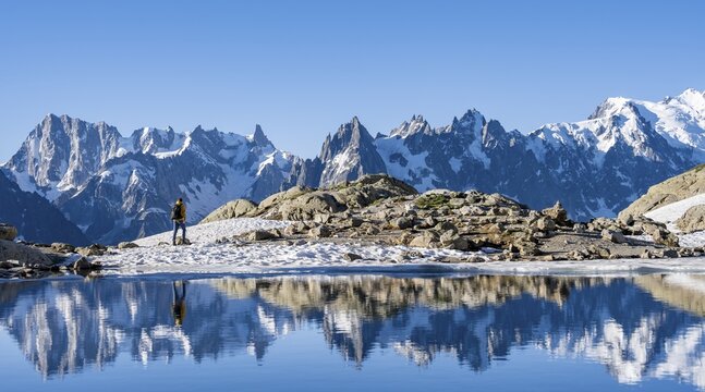 Young man hiking along a mountain lake, mountain landscape in morning light, reflection in Lac Blanc, mountain peak, Aiguille Verte, Grandes Jorasses, Aiguille du Moine, Mont Blanc, Mont Blanc Massif, Chamonix-Mont-Blanc, Haute-Savoie, France