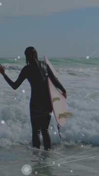 Vertical video: Surfer wading into surf with waves pushing holding pink board HUD tracking surfing