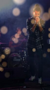 Vertical video: Lead singer after drummer beat, singing into mic for music, bokeh over singer
