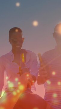 Vertical video: Friends raising beer after arm reach, toasting sunset with bokeh overlay for travel