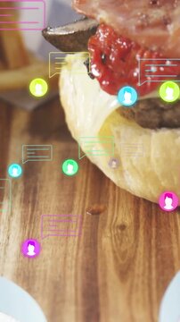 Vertical video: Top bun dropping starting burger stack as tongs placing bacon on board for promo