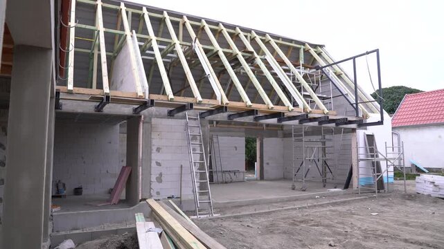 House structure with exposed roof trusses, concrete block walls, and scaffolding on a construction site