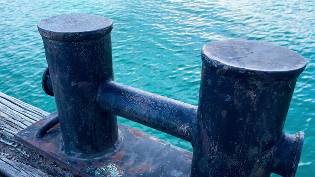 Weathered mooring bollard on a wooden dock with rippling blue water