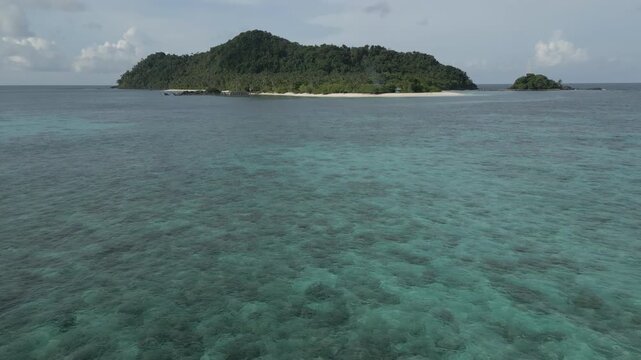 A cinematic low-altitude drone shot skimming over turquoise water before tilting up to reveal the pristine shores of Senua Island. An untouched tropical paradise in Natuna, Indonesia.