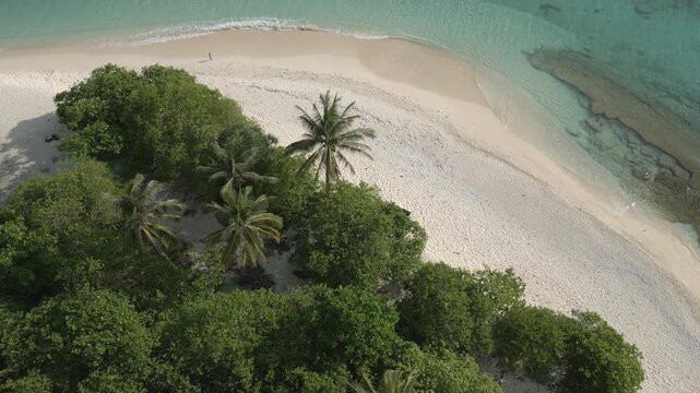 A top-down aerial drone shot flying over a dense tropical jungle to reveal a pristine white sand beach and crystal-clear ocean. A bird's-eye view of Senua Island, Natuna, Indonesia.