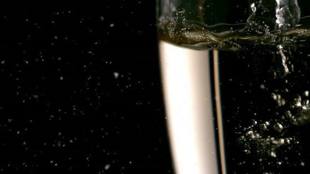 Animation of falling confetti over glass of champagne on dark background