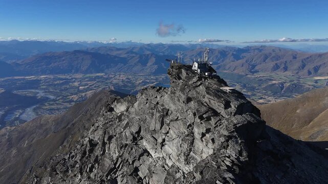 Flyover telecom tower on jagged rocky mountain summit on sunny day